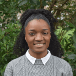 A photo of Imaan Wright - a staff member at Money and Mental Health. Imaan is smiling while standing in front of some trees.