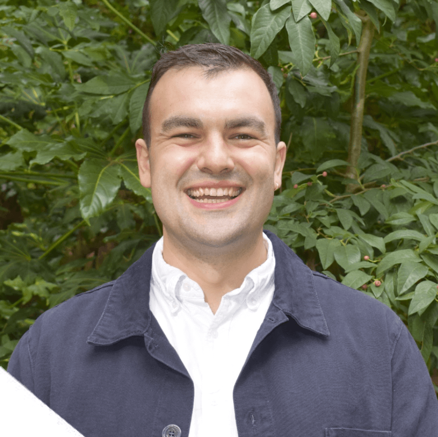 A picture of Money and Mental Health's Senior Research Officer Toby Murray, smiling while standing in front of a tree.