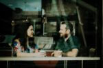 a man and a woman sitting in a coffee shop talking to each other