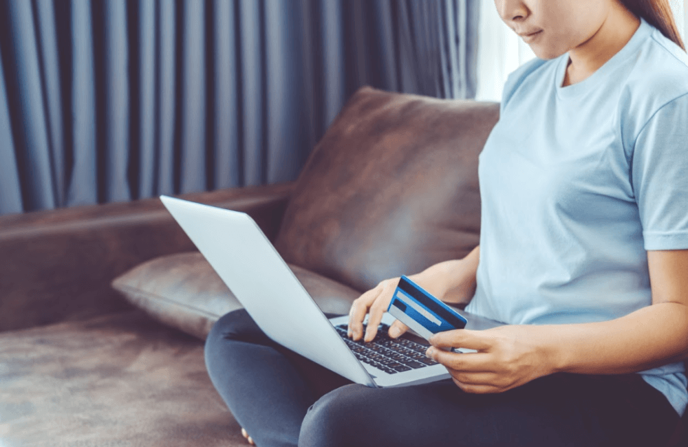Woman sitting on a couch with her laptop and holding her bank card in one hand