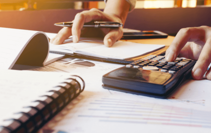 person using a calculator with a pen in one hand and notebooks on a table in front of them