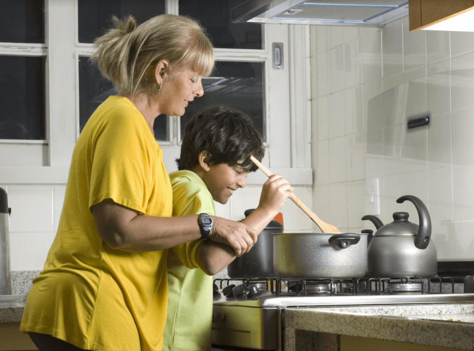 Woman helping a child to stir a pot cooking on stove