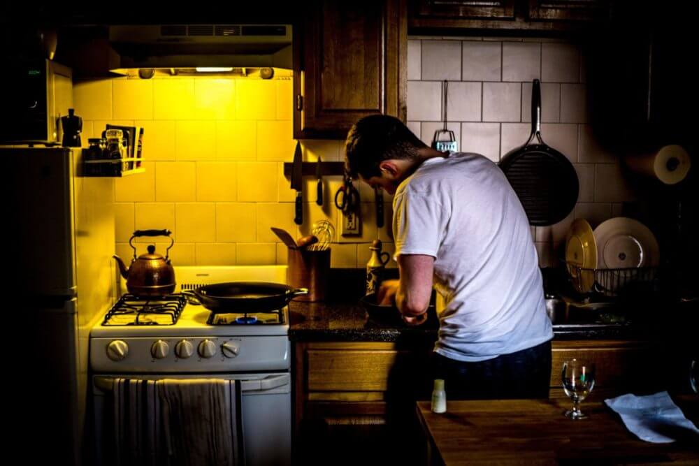 Photo of man in dark kitchen with yellow light above over