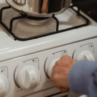 An image of someone's hand reaching to turn on a gas hob.