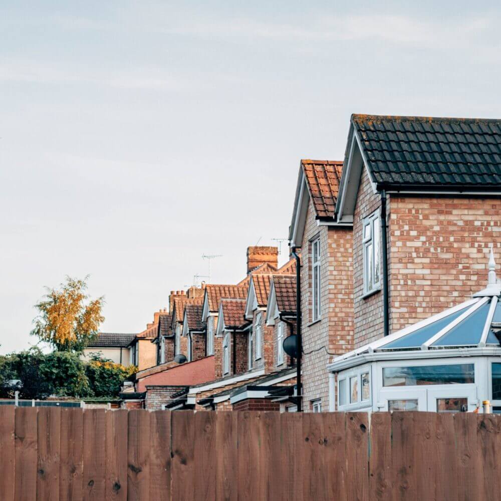 A row of houses in Ipswich, UK. The houses are brick-built and can be seen over a wooden fence.