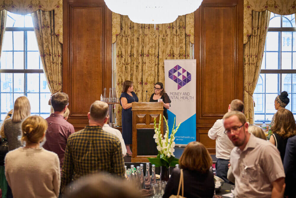 Nikki Bond and our lived experience speaker Suzanne at the podium together during Money and Mental Health's Breaking the cycle launch event
