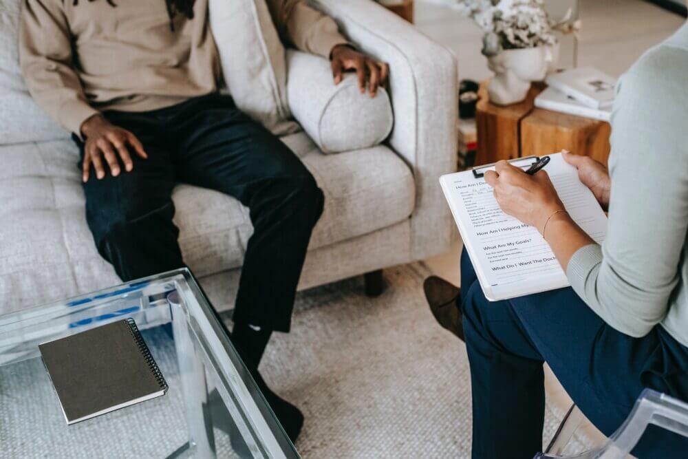 Two people face towards each other, one person taking notes.