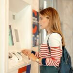 A young person in a red and white stripy jumper standing at a cash machine, holding a payment card.