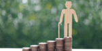 Coins in piles of ascending size with a wooden figure at the top with a walking stick.