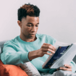 A person on an orange sofa in a blue jumper, reading.