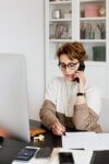 A photograph of a person holding a mobile phone to their ear while writing in a notebook.