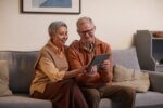 Two people sat side by side on a sofa while looking at a tablet.