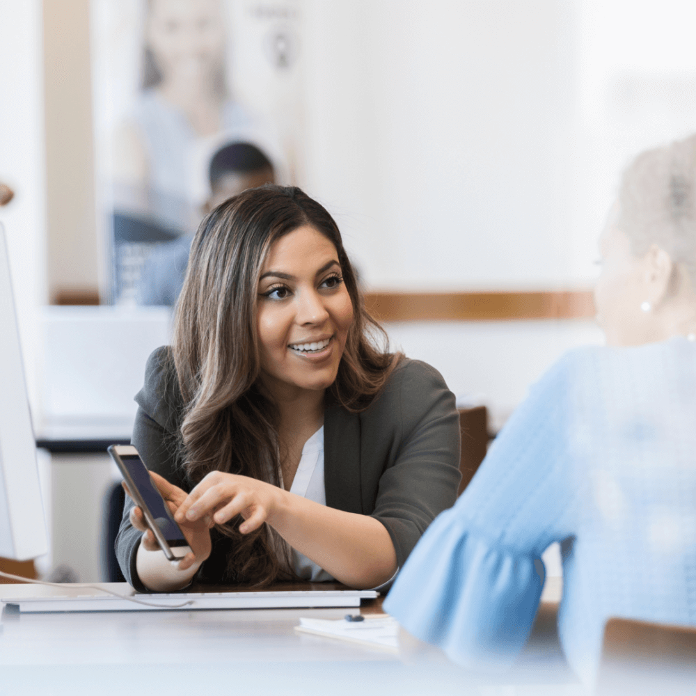 A person in a bank showing someone how to use mobile banking.