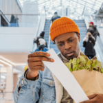 A person looking at a receipt and holding a bag of shopping.