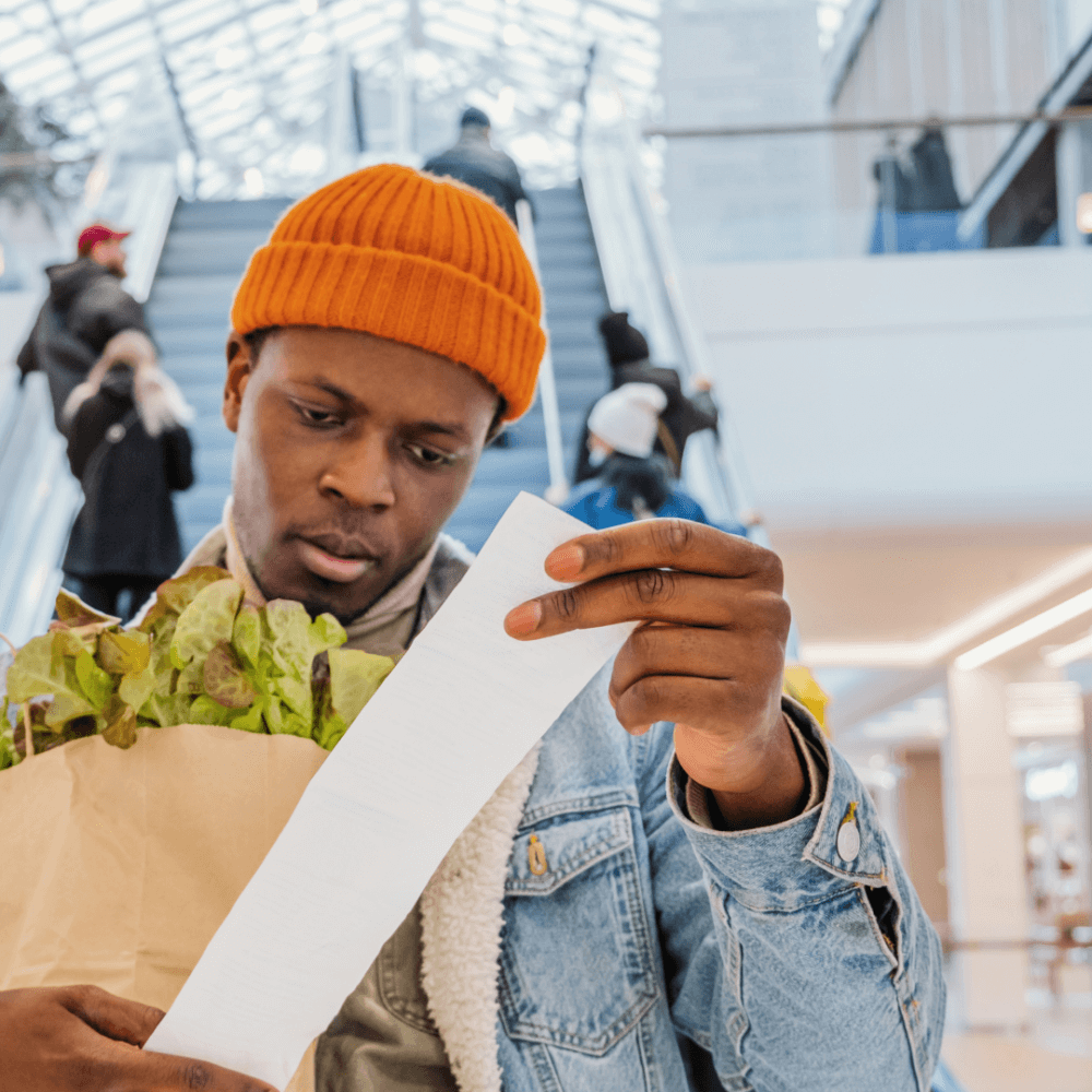 A person looking at a receipt and holding a bag of shopping.