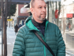 Person wearing a green jacket walking through an urban area.