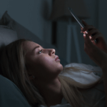 A woman lying down in darkness and looking at her mobile phone.