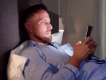 A man lying in bed looking at a mobile phone.