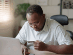 Man at a laptop looking at bank card.