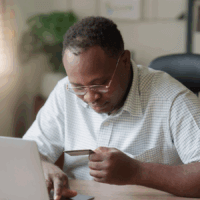 Man at a laptop looking at bank card.