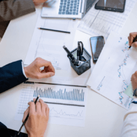 A table covered in papers and laptops. Image conveys sense of people working together to solve problems.