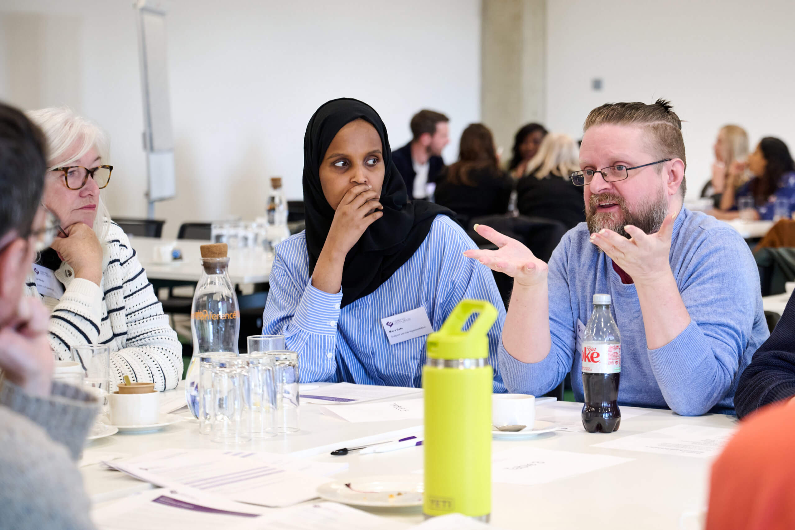 People sat talking at a table - from our event focused on improving support services alongside members of our Research Community.